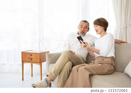ソファでくつろぎながらスマホを操作するシニア夫婦 ソファでくつろぎながらスマホを操作するシニア夫婦 131572065