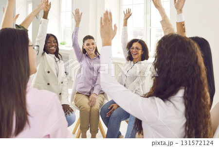 Team of diverse women sitting in a circle at a business meeting, raising their hands and voting 131572124