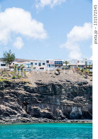 海から見える断崖絶壁の上に立つ白いリゾートホテルと地層の見える茶色のはげ山　フエルテベンテュラ島にて 131572545