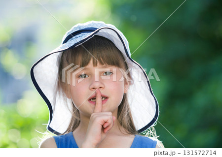 Close-up portrait of serious little girl in a big hat. Child having fun time outdoors in summer. 131572714