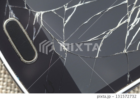 Close-up detail of black old cellphone with cracked screen on light cloth background. Gadget repair and maintenance concept. 131572732