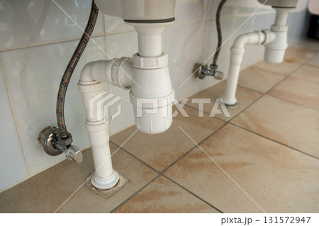 Close up of white plastic pipe drain under washing sink in bathroom. Close up of white plastic pipe drain under washing sink in bathroom. 131572947