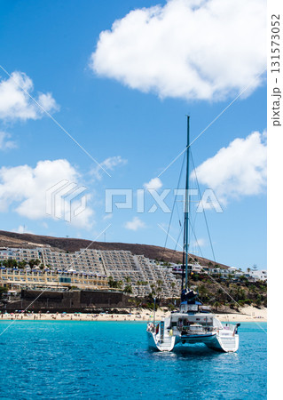 エメラルドグリーンの海のヨットと白い砂浜脇の白壁の建物と遠くに入れる裸山　フエルテベンテュラ島にて 131573052