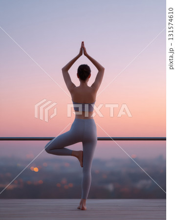 Serene young woman practicing yoga balance pose on city balcony at sunrise or sunset. peaceful and calm moment overlooking urban landscape with beautiful sky view 131574610