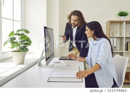 Male accountant helping his female colleague with data sheets on the office computer Male accountant helping his female colleague with data sheets on the office computer 131574863