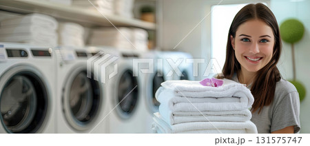 Smiling young woman holding folded towels in laundry room 131575747