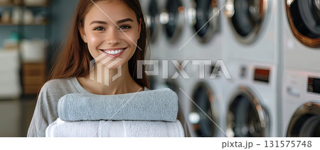 Smiling young woman holding folded towels in laundry room 131575748
