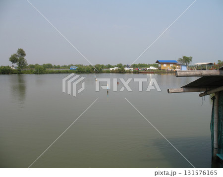 Fishing pond lake calm water rural house waterfront wooden dock blue roof tree sky reflection 131576165