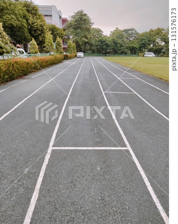 Running track lane marking leading toward school building entrance and green field under overcast sky with calm atmosphere Running track lane marking leading toward school building entrance and green field under overcast sky with calm atmosphere 131576173