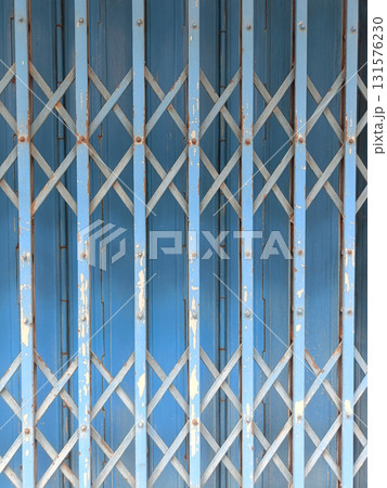 Worn blue metal folding gate with crisscross lattice pattern and peeling paint, evoking urban texture and industrial nostalgia 131576230