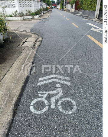 Bicycle lane road marking urban street asphalt residential neighborhood traffic symbol cyclist pavement lane arrow street curb sidewalk house fence greenery concrete painted sign quiet street road 131576242