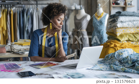 Fashion designer working her laptop studio surrounded by fabric and design sketches, contemplating her next creation with thoughtful expression 131576628
