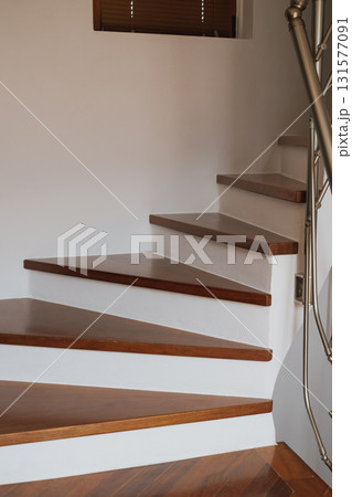 Spiral built-in staircase with brown parquet steps in interior with white walls. Spiral built-in staircase with brown parquet steps in interior with white walls. 131577091