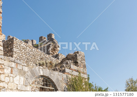 Ruins of a historic stone structure rise against a bright blue sky, highlighting the ancient craftsmanship and the beauty of nature surrounding the site 131577180