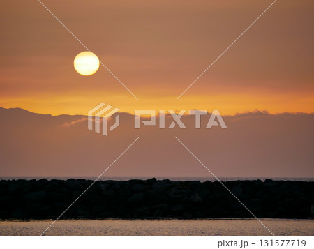 A bright sun setting over cloudy mountains, casting a warm orange glow across the sky A bright sun setting over cloudy mountains, casting a warm orange glow across the sky 131577719