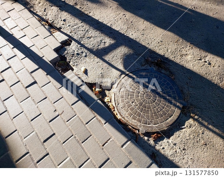 Sewer Manhole on the Street Near Sidewalk Showing Wear and Surrounding Pavement 131577850