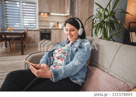 Woman relaxing on the sofa listening to music and using a smartphone Woman relaxing on the sofa listening to music and using a smartphone 131578005