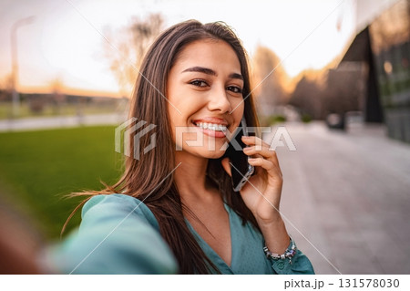 Young woman taking a selfie while talking on the phone outdoors 131578030
