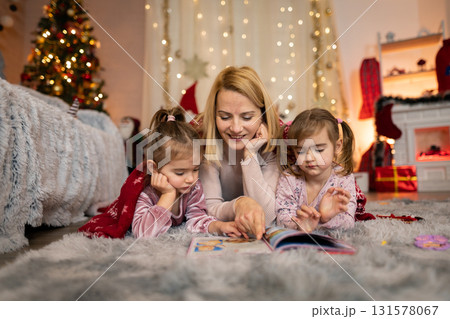 Mother reading a Christmas story to her daughters Mother reading a Christmas story to her daughters 131578067