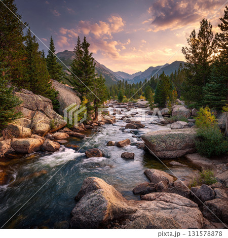 Majestic mountain landscapes at sunset, featuring a rocky river flowing through a forest with pine trees and large boulders. 131578878