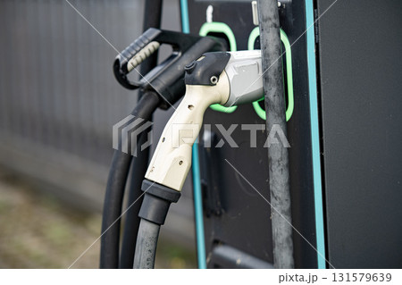 Electric Vehicle Charging Station With Dual Connectors: Close-Up Of Modern EV Power Supply Cables And Sockets With Green LED Outlines On Black Panel In Urban Setting 131579639