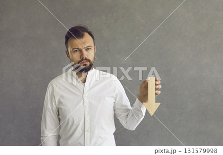 Sad business man with wooden down arrow in hand standing over studio background 131579998