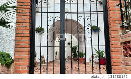 A wrought iron gate by a brick wall leads to a serene space 131580121