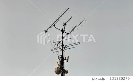 A diverse antenna array mounted on a communication tower stands prominently against a gray sky 131580279