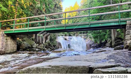 A Serene Waterfall Cascades Underneath a GreenDecorated Bridge Surrounded by a Lush Forest 131580286