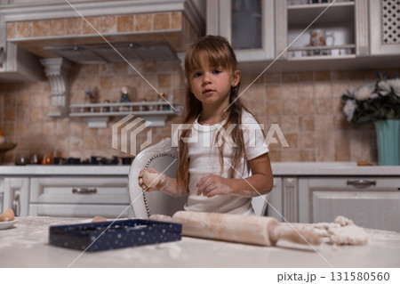 young girl is happily making a cake in a well designed kitchen. Flour covers the table as she rolls dough showcasing her enthusiasm for baking and creating delicious treats. young girl is happily making a cake in a well designed kitchen. Flour covers the table as she rolls dough showcasing her enthusiasm for baking and creating delicious treats. 131580560