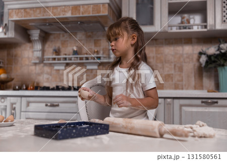 young girl joyfully prepares a cake. Flour covers the countertop while she rolls dough and carefully handles ingredients excited to bake. 131580561