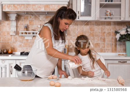 pregnant woman and her young daughter are eagerly preparing a cake. They mix ingredients and share joyful moments surrounded by kitchen tools and fresh eggs. 131580568