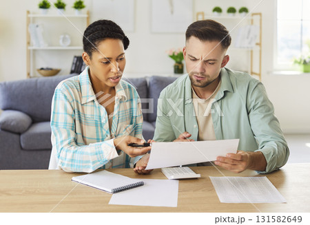 Young couple sitting on sofa and looking through financial documents at home together Young couple sitting on sofa and looking through financial documents at home together 131582649