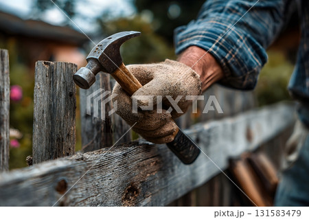 Man Repairing Broken Fence with Hammer and Nails in Backyard Man Repairing Broken Fence with Hammer and Nails in Backyard 131583479