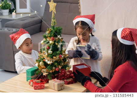 Christmas family home, parent child decorate small tree, then enjoy holiday gift box unwrapping, boy watches girl with festive Christmas cheer. Christmas family home, parent child decorate small tree, then enjoy holiday gift box unwrapping, boy watches girl with festive Christmas cheer. 131585443