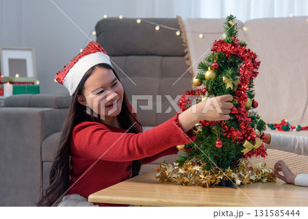 Christmas family home, young child joyfully decorating Christmas tree, parents prepare holiday gifts creating festive spirit for special Christmas day. Christmas family home, young child joyfully decorating Christmas tree, parents prepare holiday gifts creating festive spirit for special Christmas day. 131585444