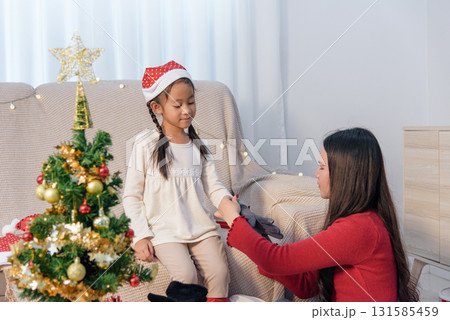 Christmas family home, parent child exchanging gift near holiday tree, festive spirit filling room during warm Christmas celebration, joyful holiday moments. Christmas family home, parent child exchanging gift near holiday tree, festive spirit filling room during warm Christmas celebration, joyful holiday moments. 131585459