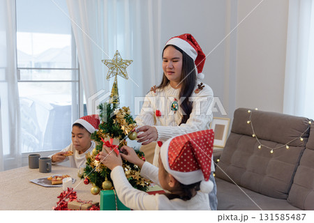 Christmas family home, parent guides child decorating holiday Christmas tree, young girl placing ornaments, boy enjoys meal, gifts are ready for celebration. Christmas family home, parent guides child decorating holiday Christmas tree, young girl placing ornaments, boy enjoys meal, gifts are ready for celebration. 131585487