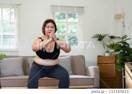Strength Training and Empowerment. A woman confidently performing a squat exercise at home, building her strength. 131585623