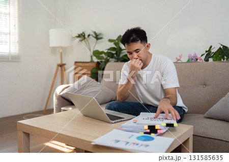 Remote Work and Focus. A man working from home, thoughtfully assessing information on his laptop and papers. Remote Work and Focus. A man working from home, thoughtfully assessing information on his laptop and papers. 131585635
