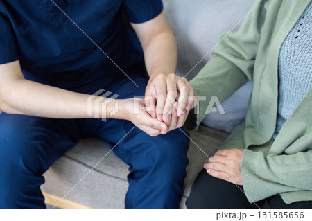 Patient Care and Emotional Connection. A healthcare professional demonstrates empathy by holding the hand of an elderly patient during a home visit. Patient Care and Emotional Connection. A healthcare professional demonstrates empathy by holding the hand of an elderly patient during a home visit. 131585656