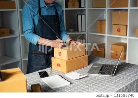 Businessperson labeling multiple packages while using a laptop in a well-organized workspace. Businessperson labeling multiple packages while using a laptop in a well-organized workspace. 131585740