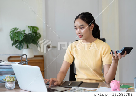 Online Payment and Budget Planning. A young woman managing her finances while holding a calculator and looking at her laptop. Online Payment and Budget Planning. A young woman managing her finances while holding a calculator and looking at her laptop. 131585792