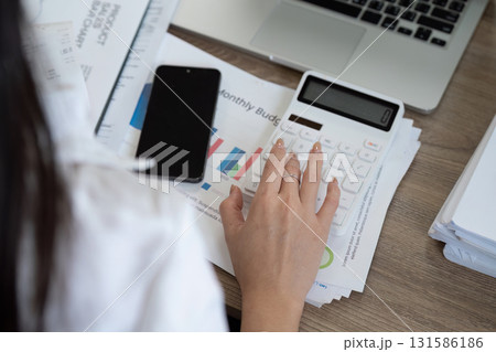 Detail-oriented financial analyst calculating budget using a calculator and reviewing financial reports. 131586186