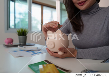 Saving Money: Woman Depositing Coins into Piggy Bank 131586399