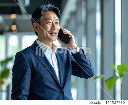 50代の日本人中年ビジネスマン、オフィスでスマートフォンを耳に当て、真剣な表情で通話する 131587680