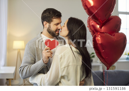Happy couple in love, man, woman kissing holding red heart symbol, balloons for romantic Valentine Happy couple in love, man, woman kissing holding red heart symbol, balloons for romantic Valentine 131591186