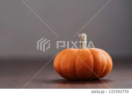 Small orange pumpkin on black walnut table with white wall background 131592770