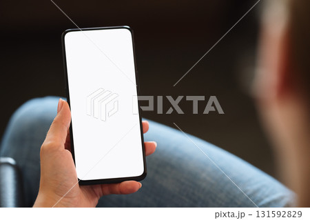 Young woman sitting in chair with modern smartphone with white screen Young woman sitting in chair with modern smartphone with white screen 131592829