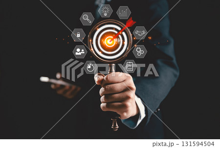 Businesswoman uses magnifying glass to focus on target board icon, symbolizing business concept of strategic planning, goal achievement, and innovation, key drivers of success in modern enterprises. 131594504